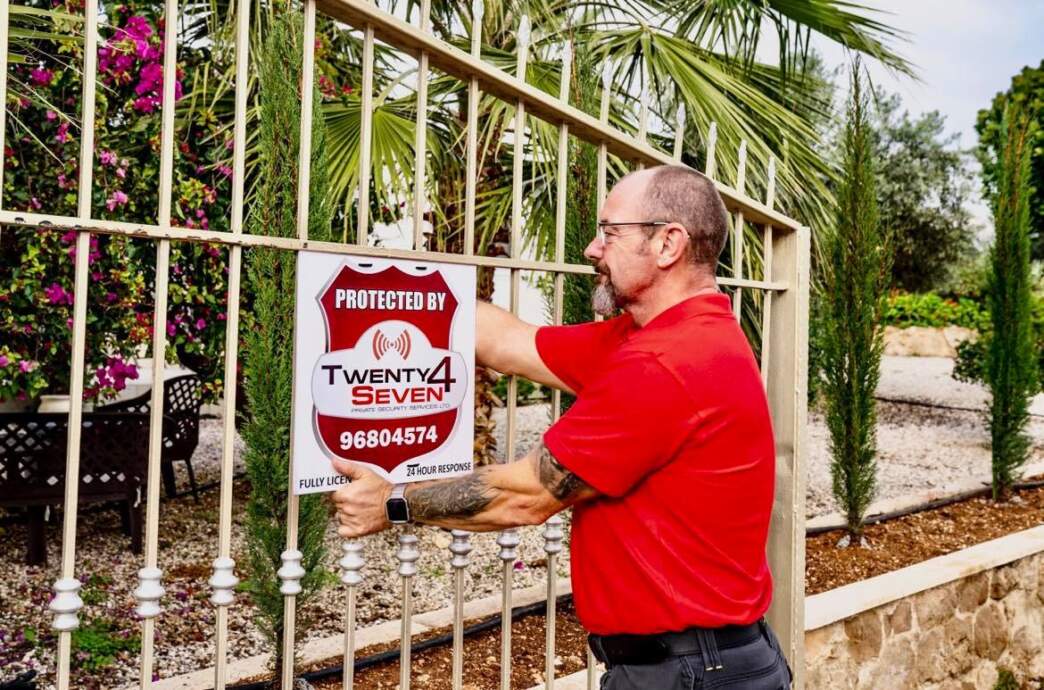 A Twenty4Seven engineer fixing a Protected By Twenty4Seven sign to a villa gate in Paphos